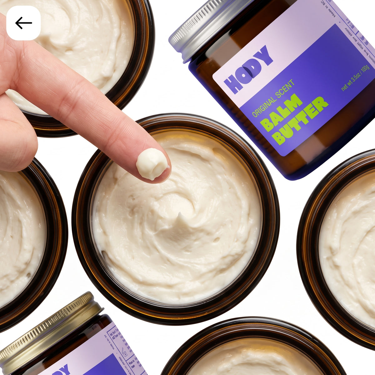 A finger scooping whipped HODY Balm Butter from an open jar, surrounded by more open jars and a jar of Original Scent